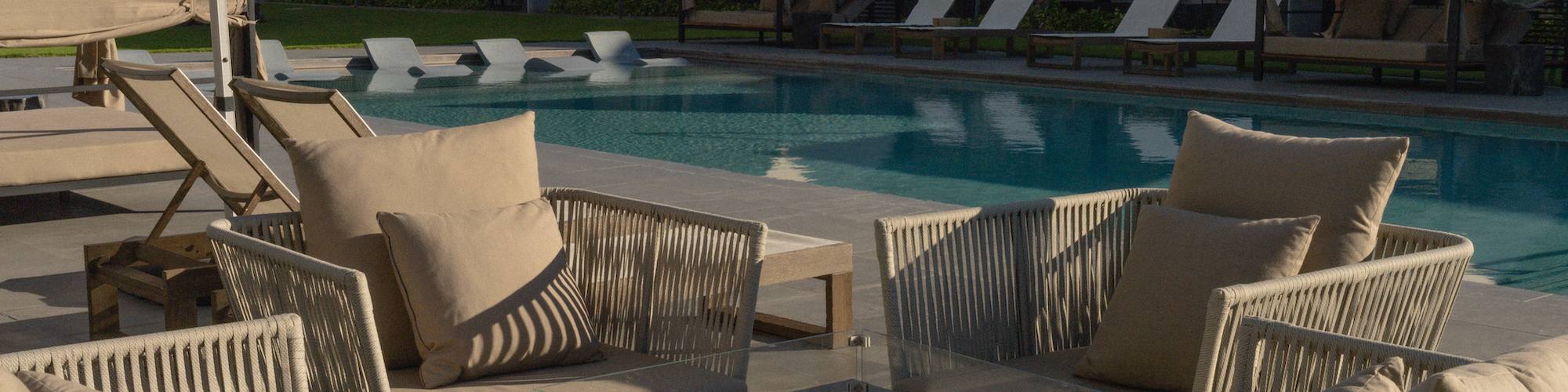 Outdoor seating near a pool with cushioned chairs and umbrellas; cabanas and loungers are in the background by the swimming pool.