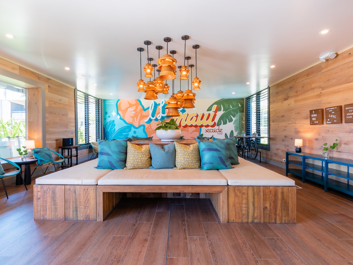 A stylish room with wooden accents features a large central seating area, colorful mural, and hanging lights, creating a cozy ambiance.