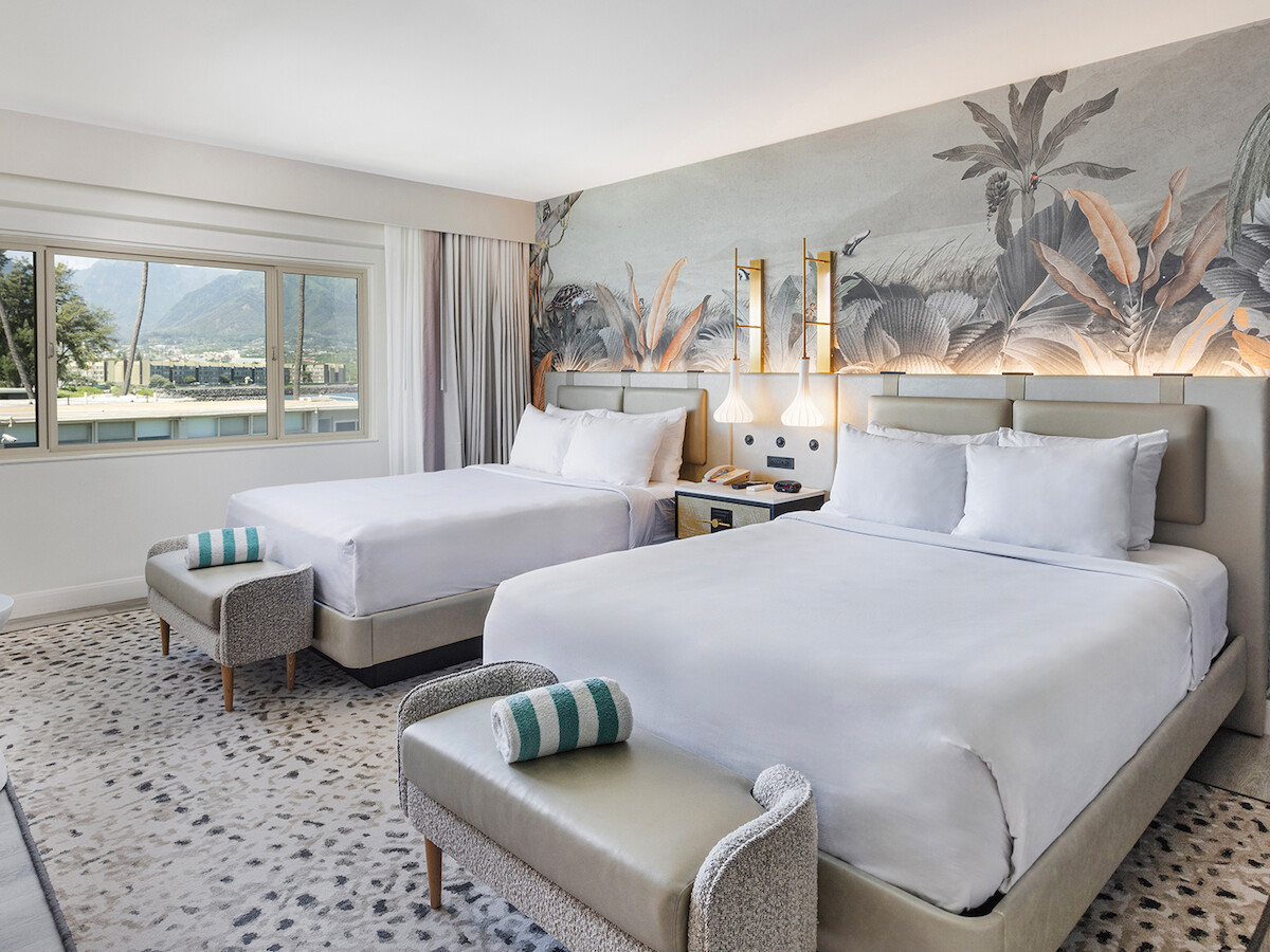 The image shows a hotel room with two double beds, floral wallpaper, a window view, a side table, and stylish decor.