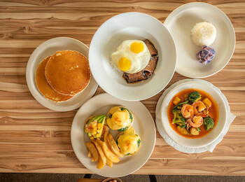 The image shows a table with pancakes, eggs on toast, a rice dish, eggs benedict with potatoes, and a vegetable stew.