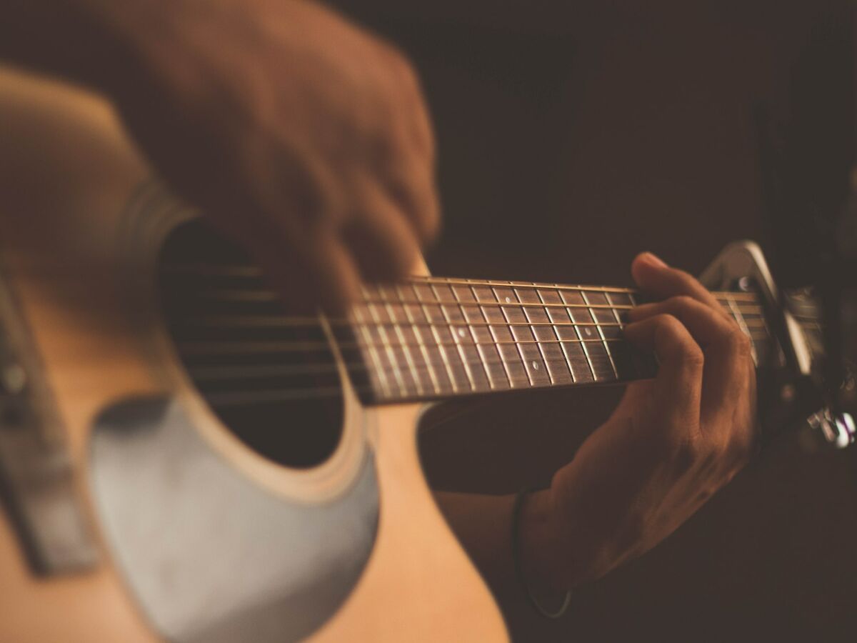 A close-up view of a person playing an acoustic guitar, with focus on their hands and the instrument's strings and body.