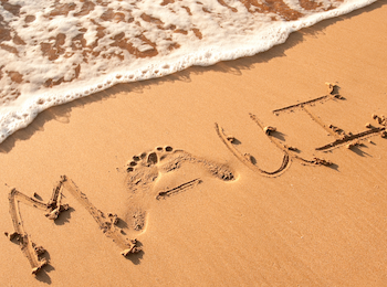 "Maui" is written in the sand near the shoreline, with ocean waves approaching.